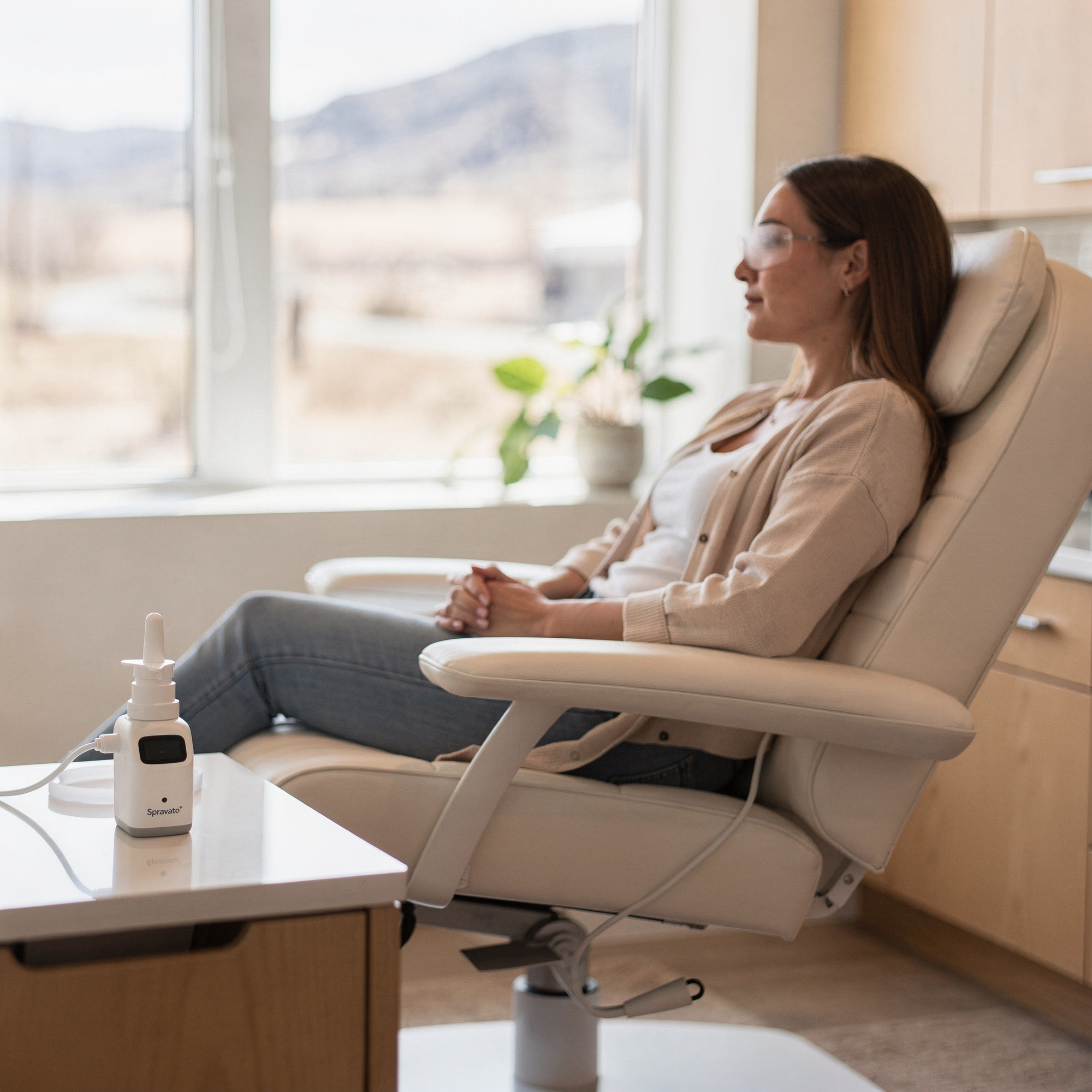 Patient seated in a reclined chair during Spravato treatment with a nasal device on the table beside her